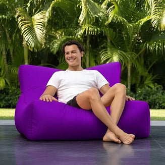 Person sitting on a purple bean bag chair outdoors with greenery in the background