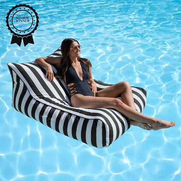 Woman lounging on a black and white striped bean bag pool float in clear blue water.