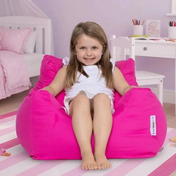 Young girl sitting on a pink bean bag chair in a child's bedroom.