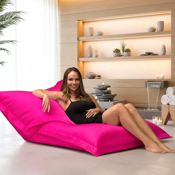 Woman sitting on a pink bean bag chair in a spa-like setting with shelves and plants.
