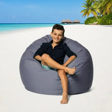 Child sitting on a bean bag chair on a tropical beach with palm trees and clear blue water.